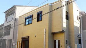 A modern two-story building with a beige facade, large windows, and a visible entrance with steps. - HANASTAY YAMA (Osaka)