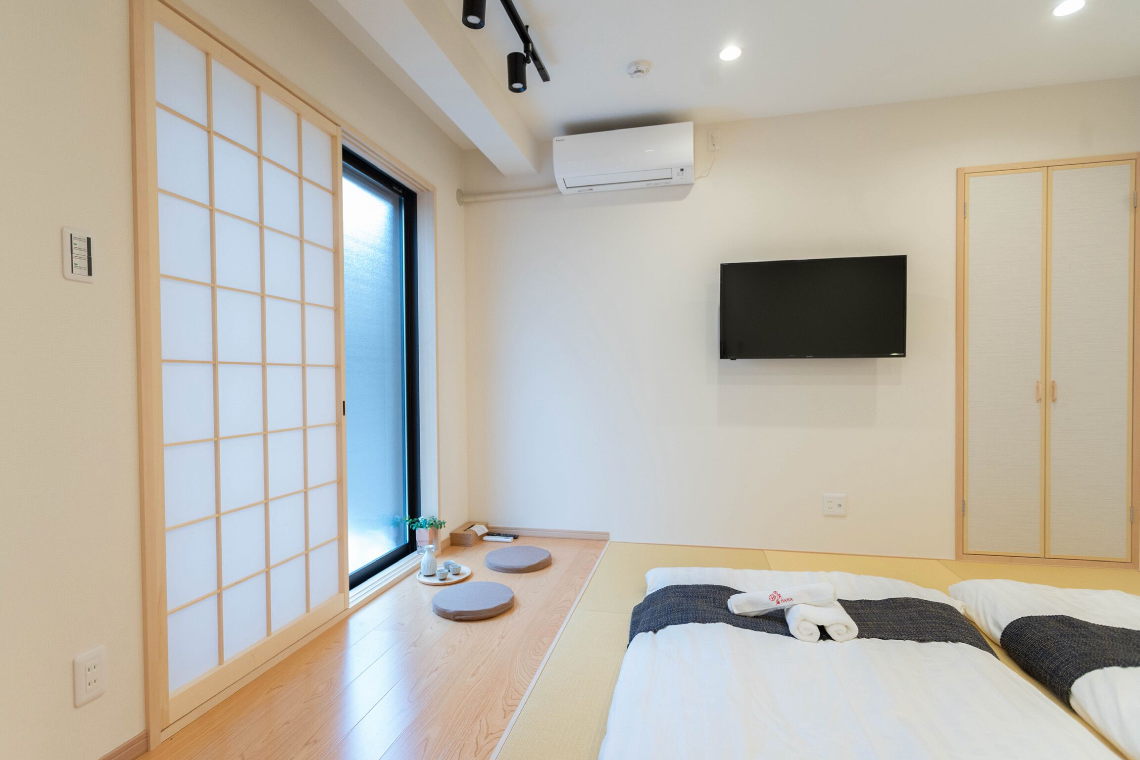 A hotel room with tatami flooring, a sliding door, a flat-screen TV, and a bed with pillows and a towel.