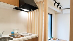 A modern kitchen with wooden cabinets, a black range hood, and a window with vertical blinds. - HANASTAY YAMA (Osaka)