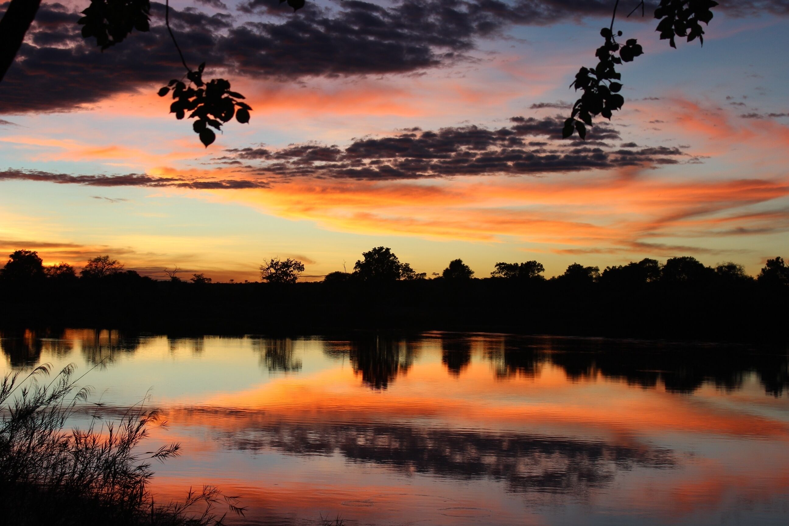 A sunset over a calm lake with silhouettes of trees and a clear reflection on the water.