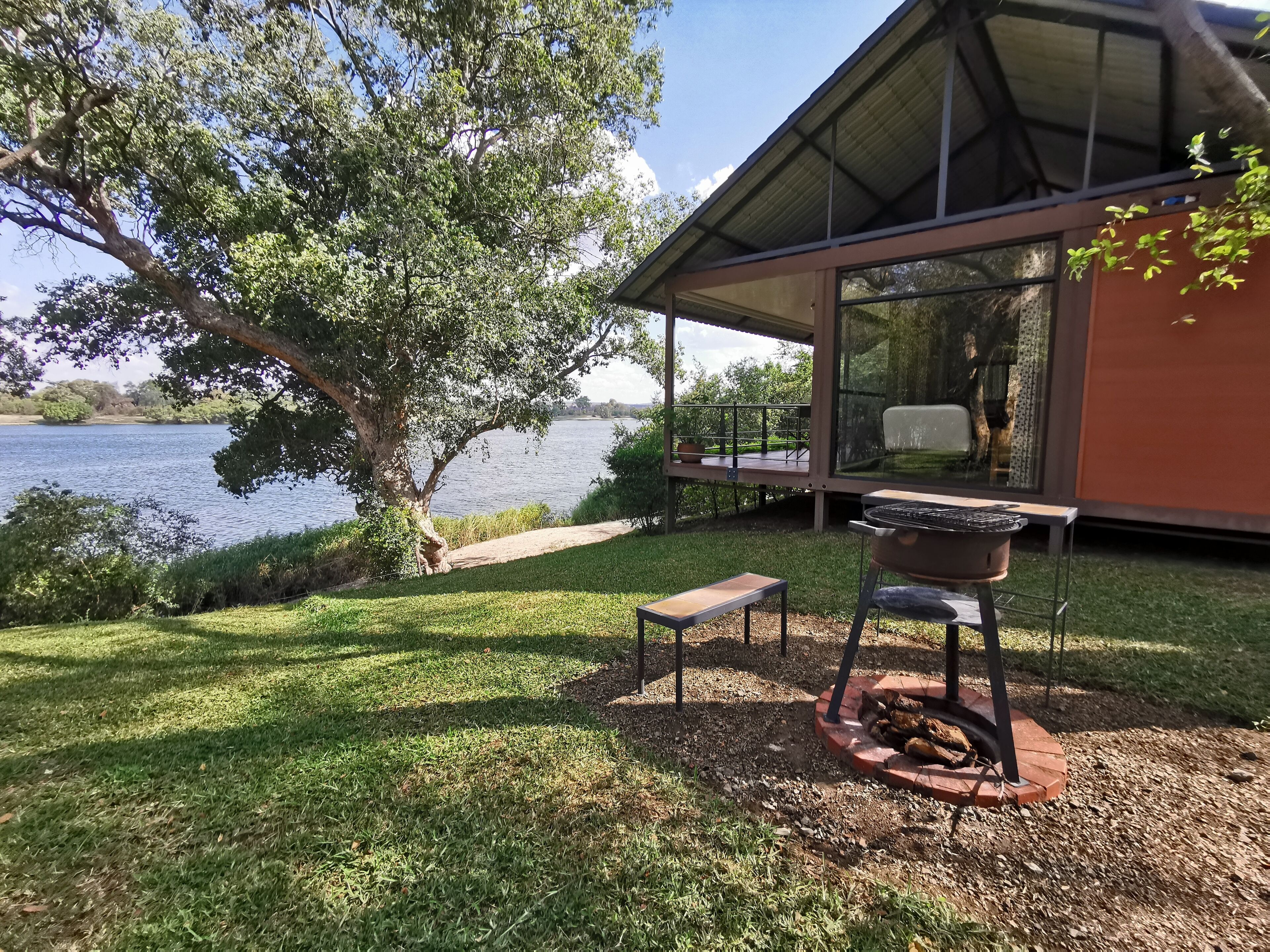 A covered outdoor area with a grill, a bench, and a view of a lake.