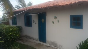 A white building with a blue door and windows, surrounded by greenery.