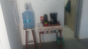 A small kitchenette area with a water dispenser, a coffee maker, and a table with a tea set.
