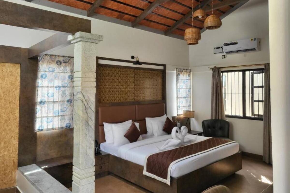 Habitación de hotel con una cama grande, cabecero, ventana con cortinas, aire acondicionado montado en la pared y techo con vigas a la vista.