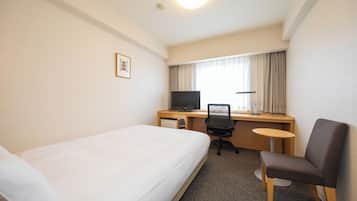 Habitación de hotel con una cama individual, un escritorio con computadora y silla, y una mesita pequeña.