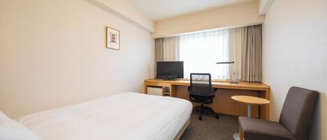 Habitación de hotel con una cama individual, un escritorio con computadora y silla, y una mesita pequeña.