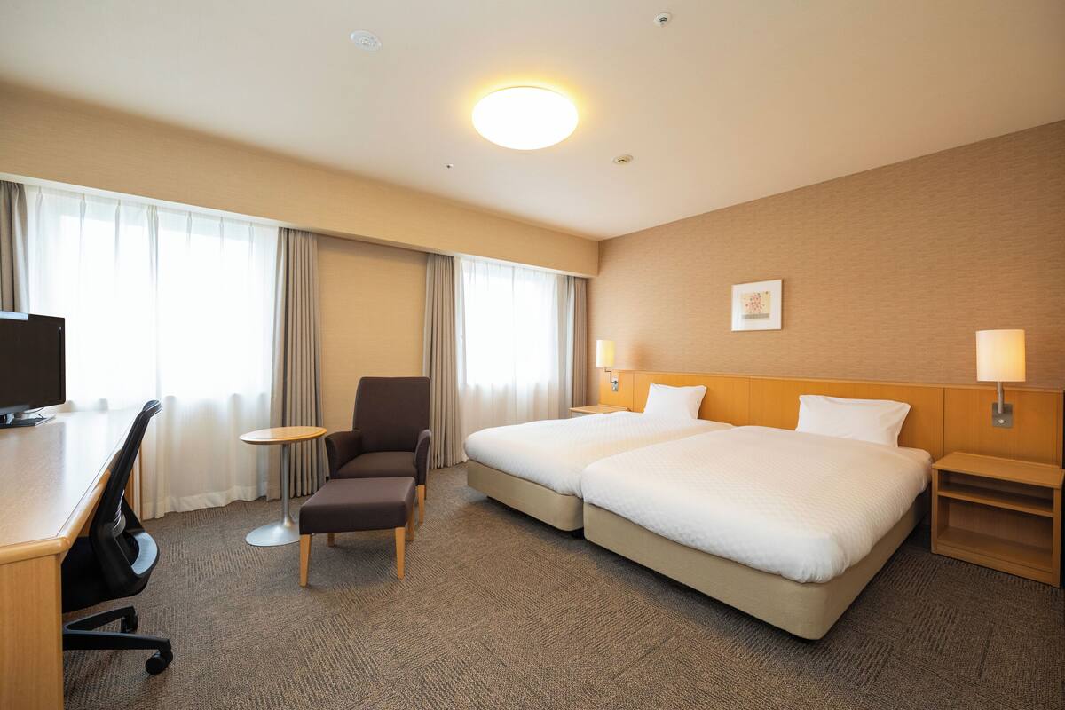 Habitación de hotel con dos camas, un escritorio, una silla, una mesita y un televisor.