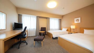 Una habitación de hotel con escritorio, dos camas, una silla, una mesita y una lámpara.