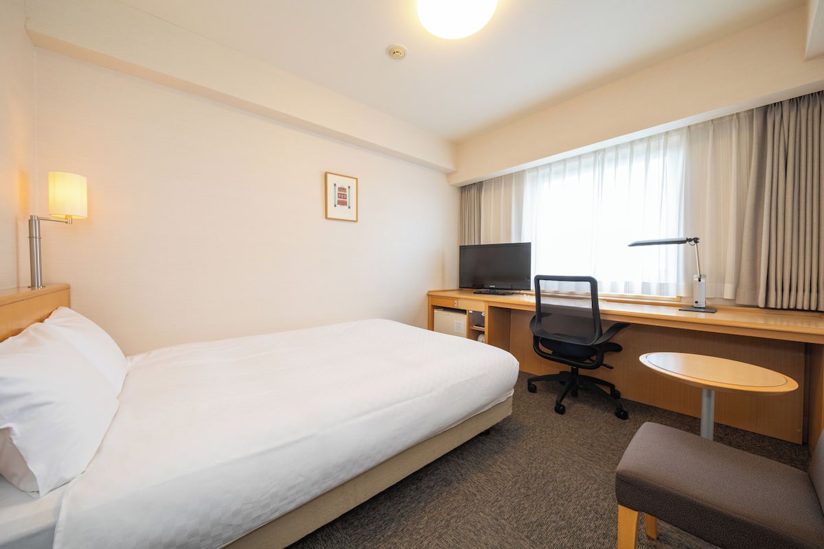 Habitación de hotel con una cama individual, un escritorio con ordenador, una silla y una mesita redonda.
