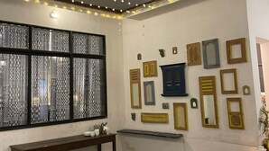 A room with a high ceiling, string lights, a bench, a table, wicker chairs, and a wall with various framed items. - Villa 108 Amarja's Sierra Vista (Mawal)