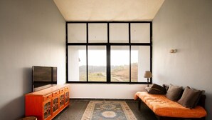 A room with a large window, a television, a sofa, a cabinet, and a patterned rug. - Villa 108 Amarja's Sierra Vista (Mawal)
