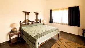 Un dormitorio con cama, mesitas de noche, una ventana con cortinas y una colcha estampada.