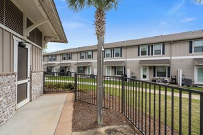 A multi-story residential building with a brick facade, a palm tree, and a black metal fence.