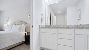 Une chambre à coucher comprenant un lit, une table de chevet, un grand miroir et une salle de bain avec un meuble-lavabo et un évier.