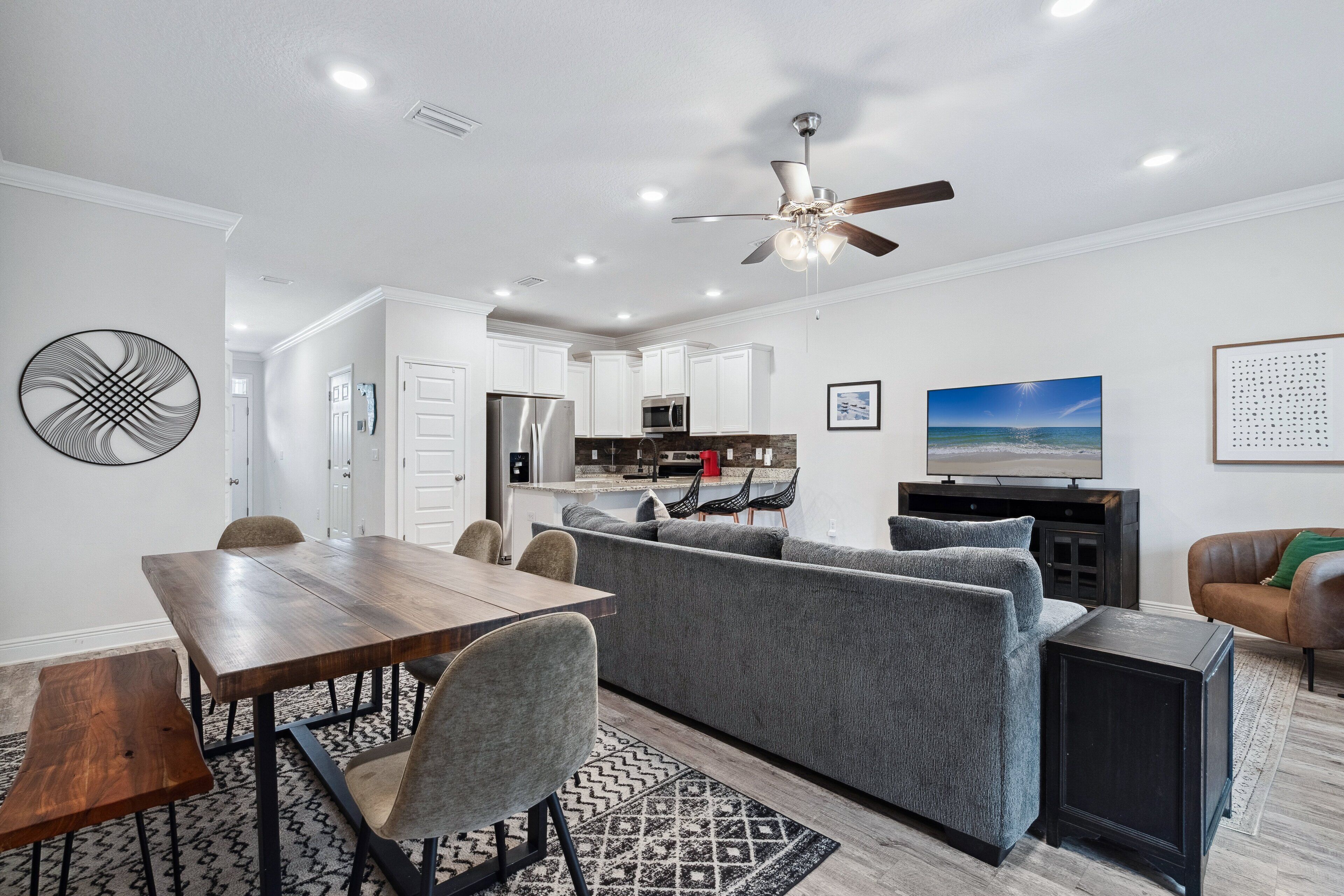 A modern living room with a dining area, grey sofa, and a kitchen in the background.