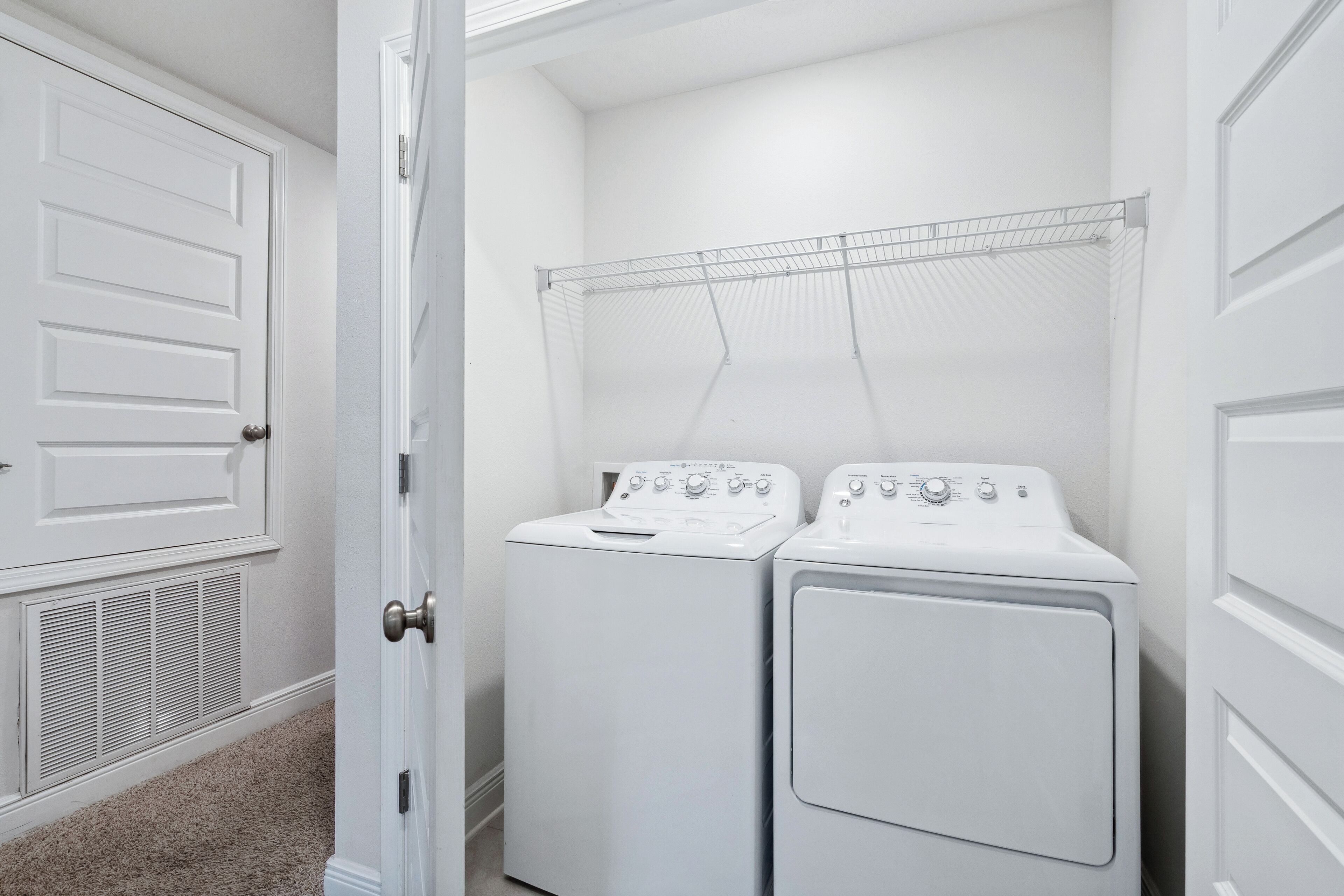 A laundry room with two stacked washers and dryers, a drying rack, and a vented dryer.
