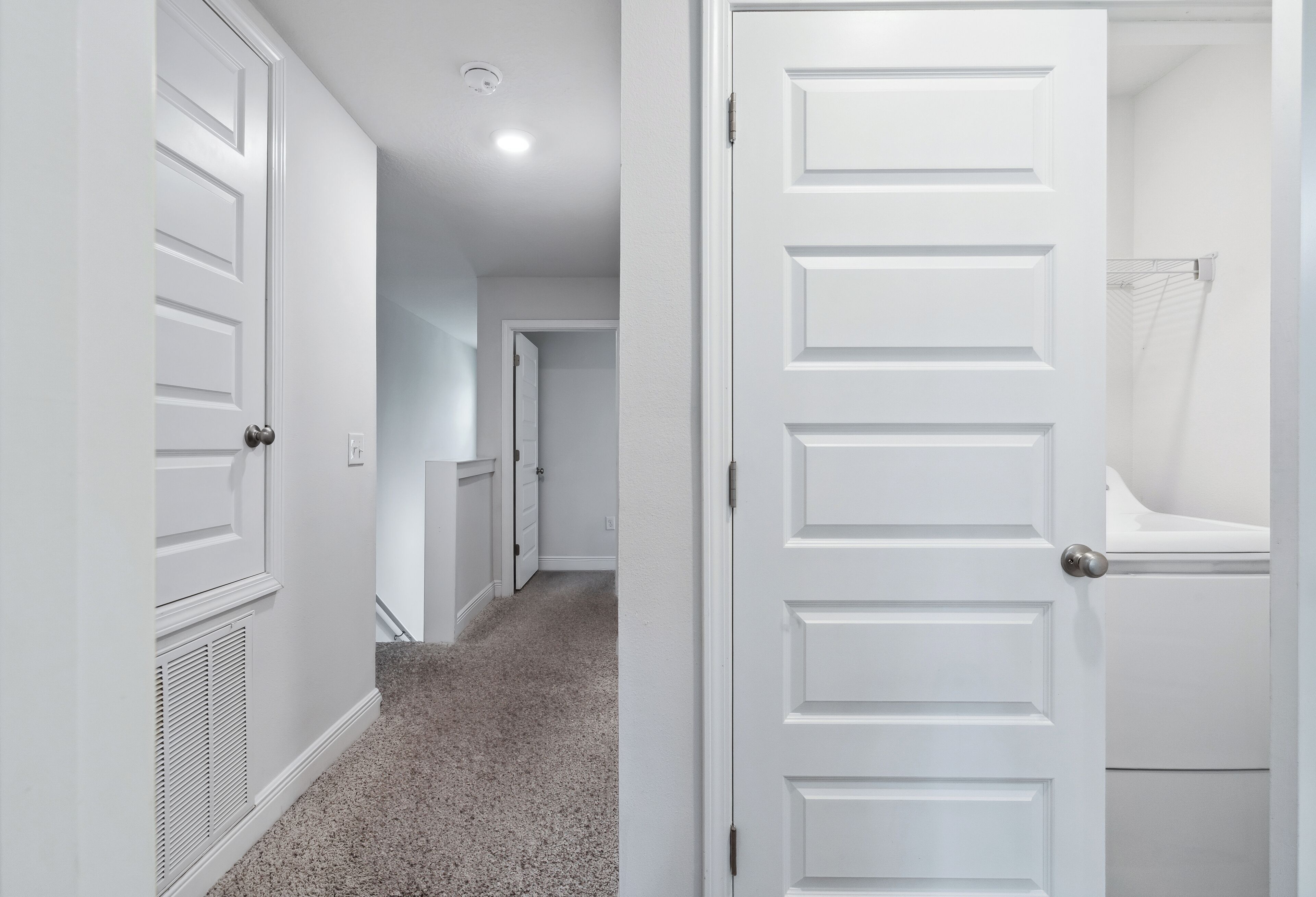 A hallway with white doors, a vent, and a carpeted floor.