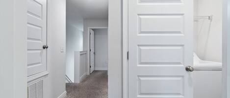 A hallway with white doors, a vent, and a carpeted floor.