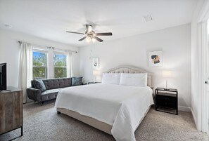 A bedroom with a large bed, a ceiling fan, a sofa, and a TV.
