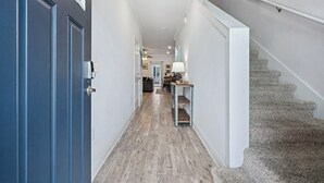 Un couloir avec une porte bleue, un escalier et, au fond, un coin repas.