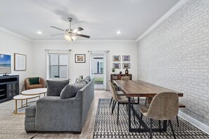 A modern living room with a gray sofa, a wooden dining table, and a ceiling fan.