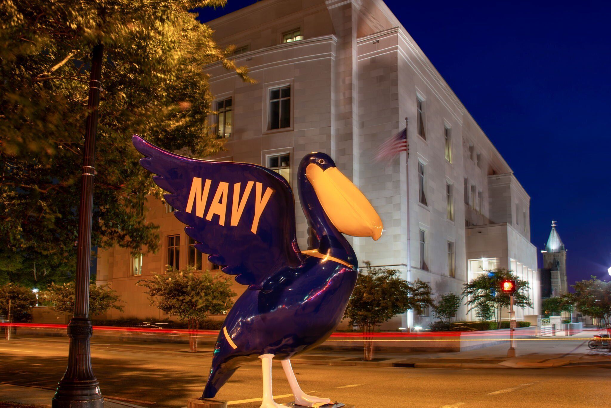 Een groot beeld van een vogel met het woord “NAVY” op de vleugels, voor een gebouw met een klokkentoren.