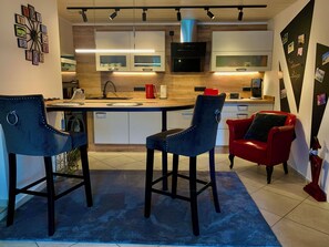 Une cuisine moderne avec un îlot central, deux tabourets de bar, une chaise rouge et un four à micro-ondes.