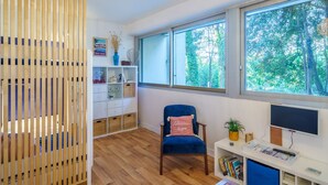 A room with a large window, a blue chair, a white desk, and a wooden partition.