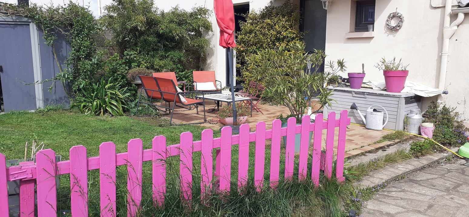 En have med et pink hegn, et bord med stole og plantekrukker.