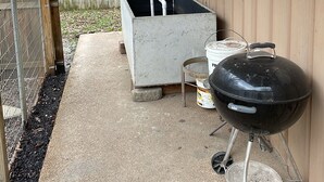 Un espace extérieur aménagé en patio, doté d’un sol en béton, d’un barbecue, d’une poubelle et d’une clôture en bois.