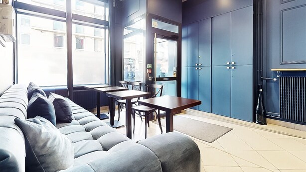 A modern living room with a sofa, dining table, and chairs. There are large windows and a view of the street outside.