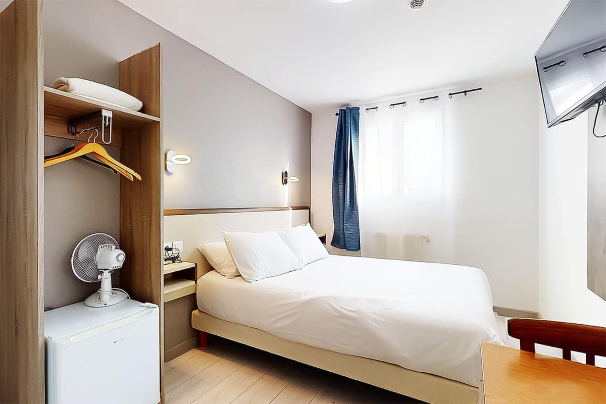 A modern hotel room with a bed, a bedside table, a wardrobe, and a wall-mounted TV.