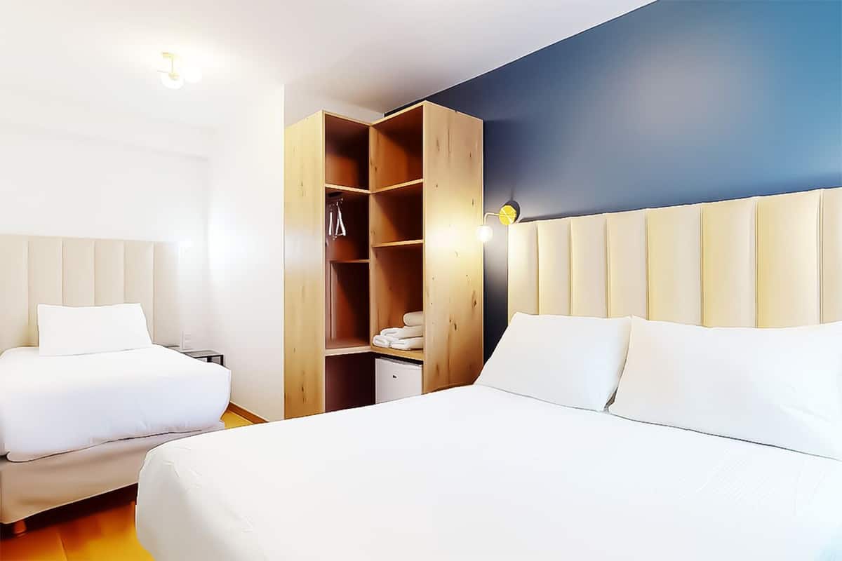 A hotel room with two beds, a wooden wardrobe, and a blue accent wall.
