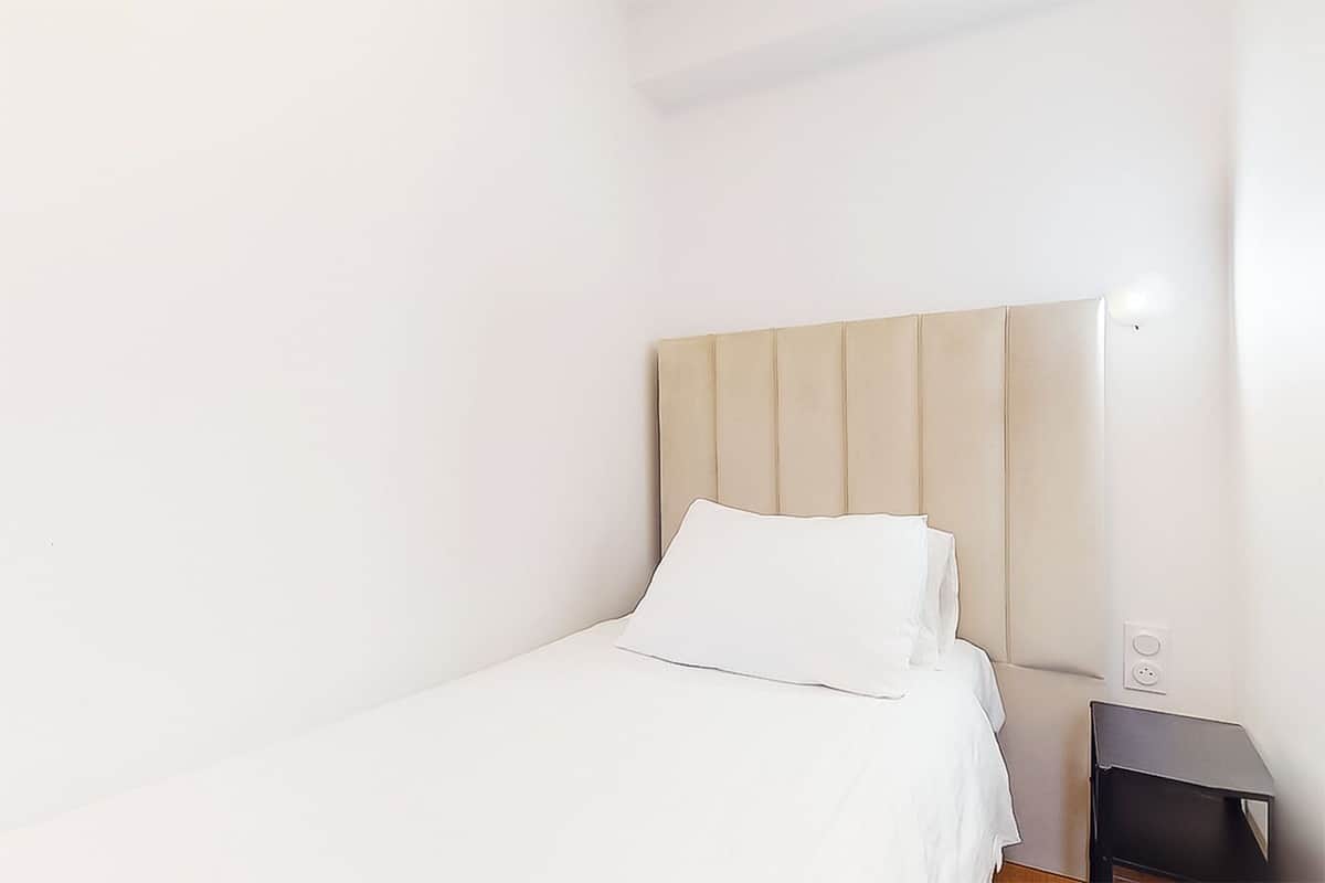 A simple, clean room with a bed, a nightstand, and a wall socket.