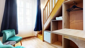 A room with a teal armchair, a wooden staircase, and a wardrobe with hanging space.