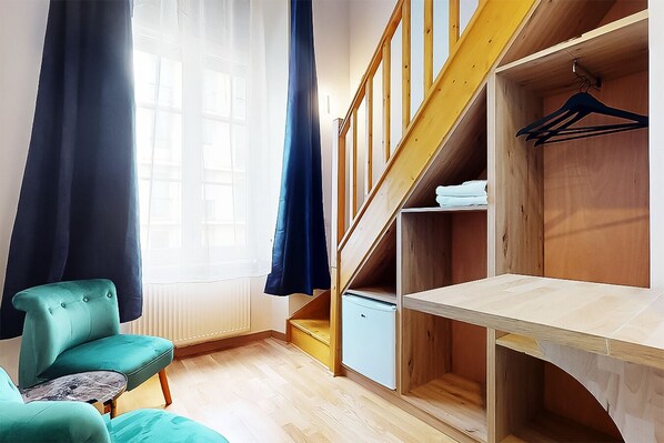 Une pièce avec un fauteuil de couleur turquoise, un escalier en bois et une armoire avec une tringle pour suspendre les vêtements.