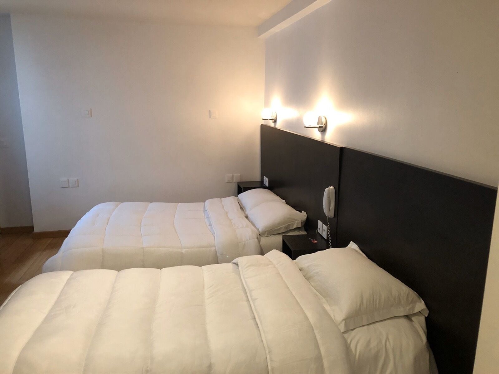A hotel room with two beds, each with a headboard and bedside tables.