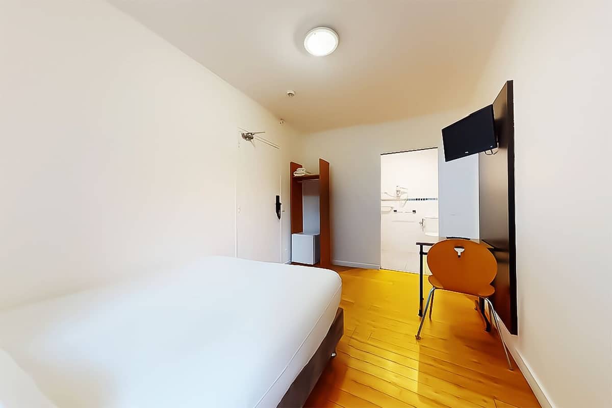 A hotel room with a bed, a chair, a desk, and a bathroom visible through an open door.