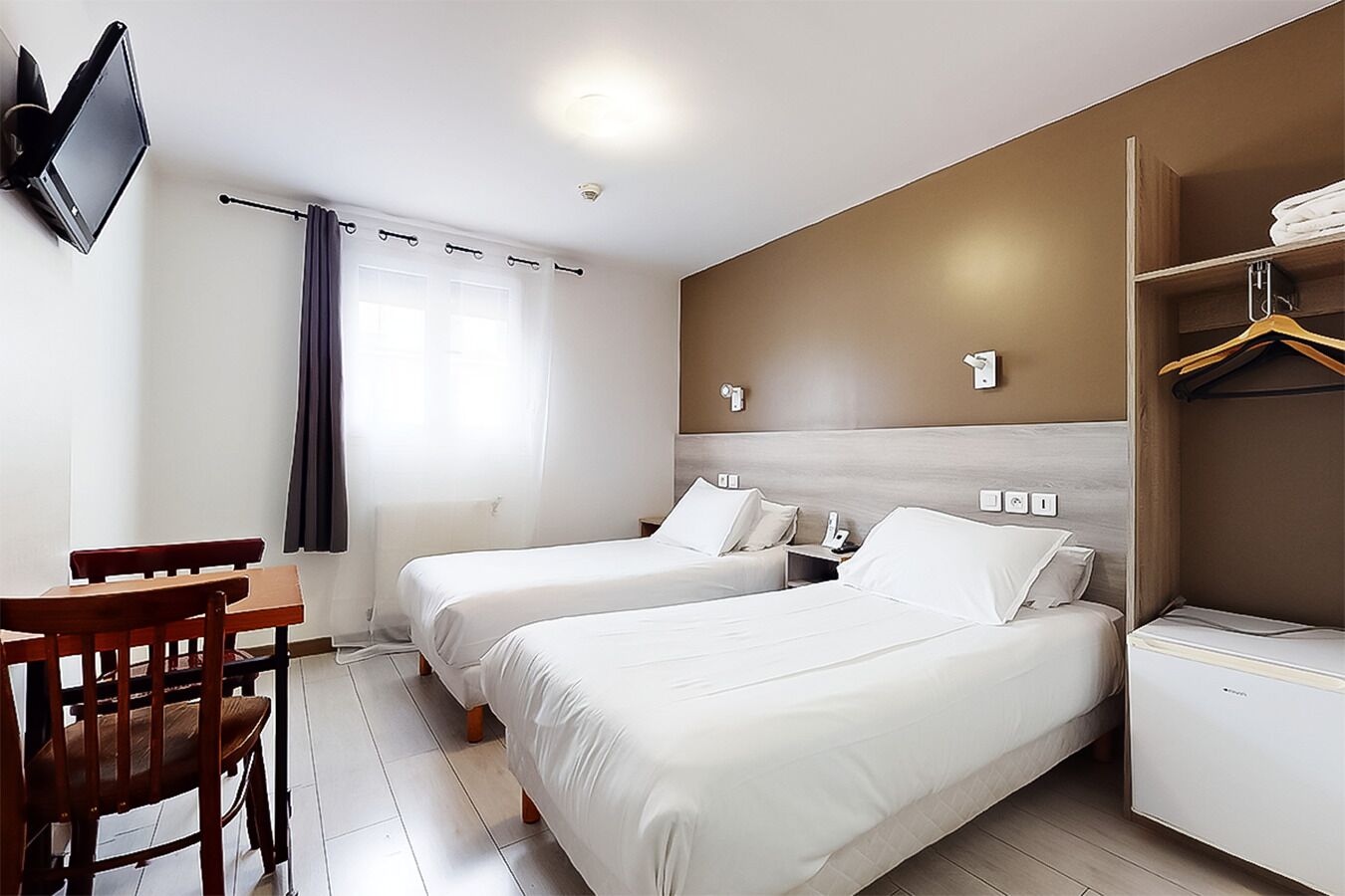 Une chambre d’hôtel avec deux lits, un bureau et un téléviseur fixé au mur.