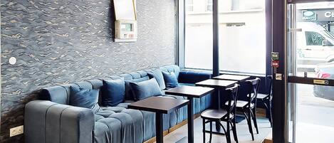 A modern interior with a blue sofa and tables, a patterned wall, and a view of the street outside.
