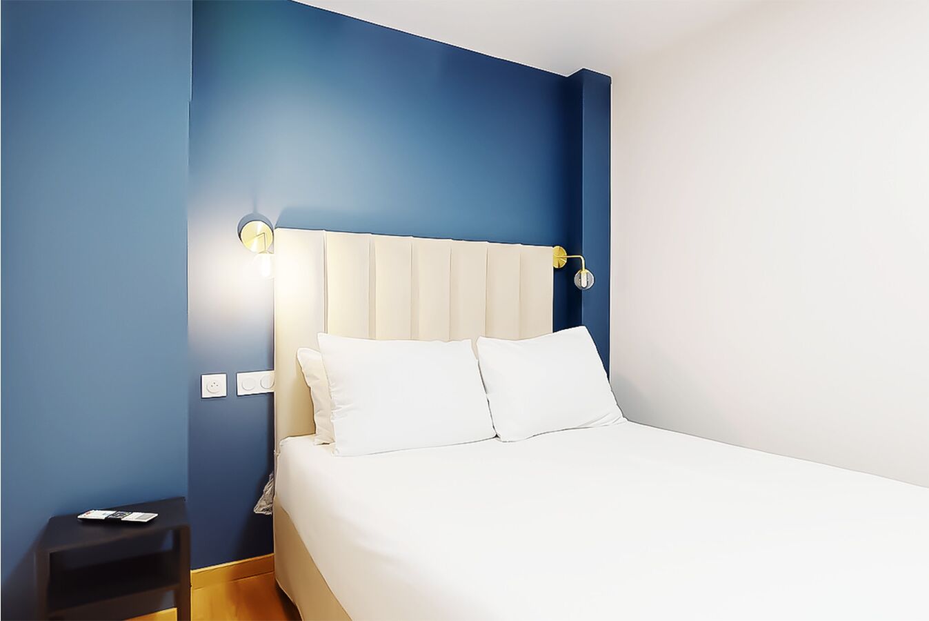 A bedroom with a bed, a nightstand, and a wall socket.