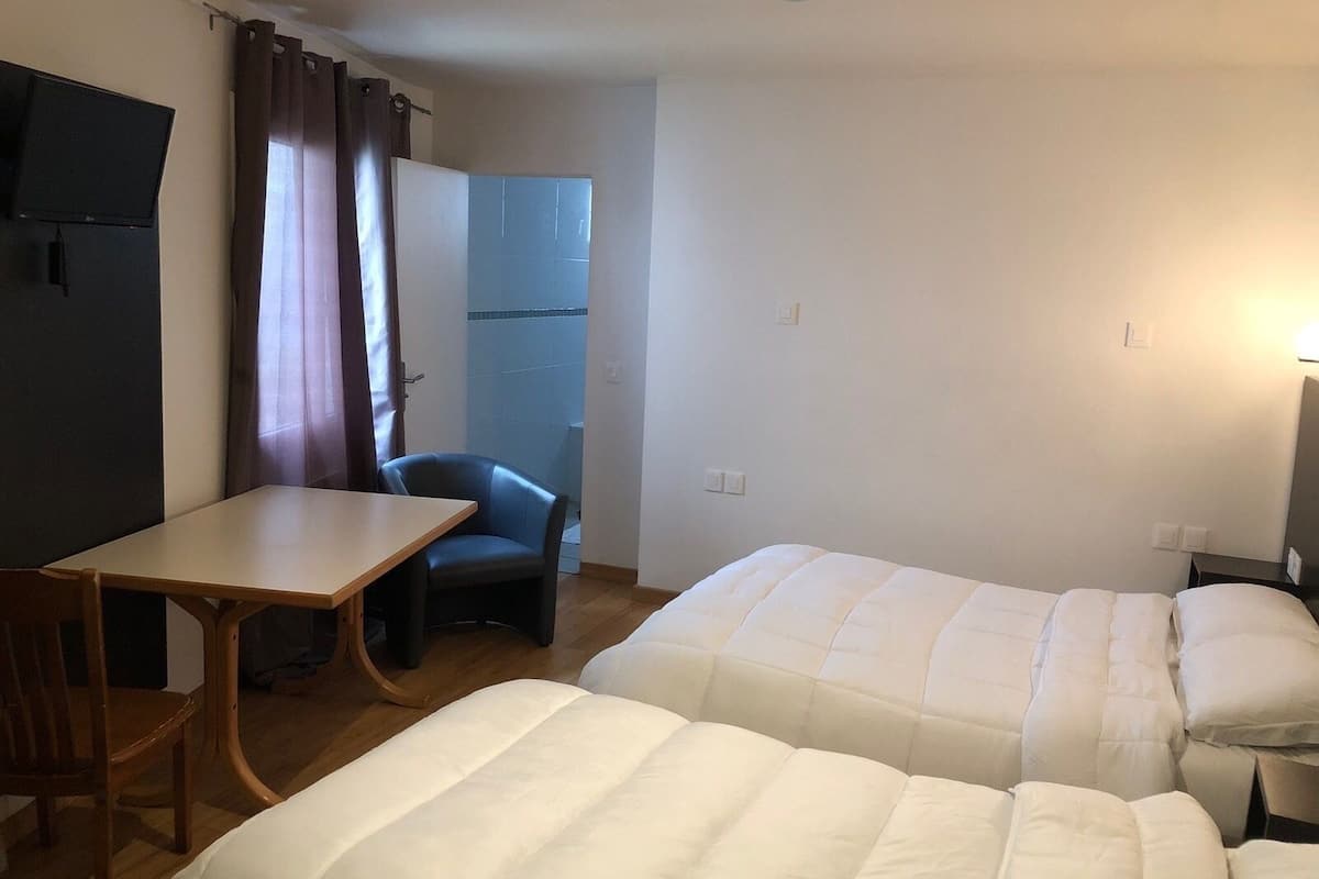 A small, simple room with two beds, a desk, and a chair.
