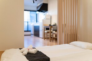 A neatly made bed with a rolled towel and a dark blanket in a hotel room. - HANASTAY MATSU (Osaka)