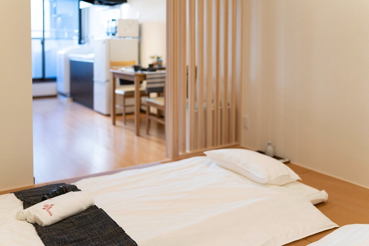 A hotel room with a bed, a pillow, a towel, and a small table with a bottle.
