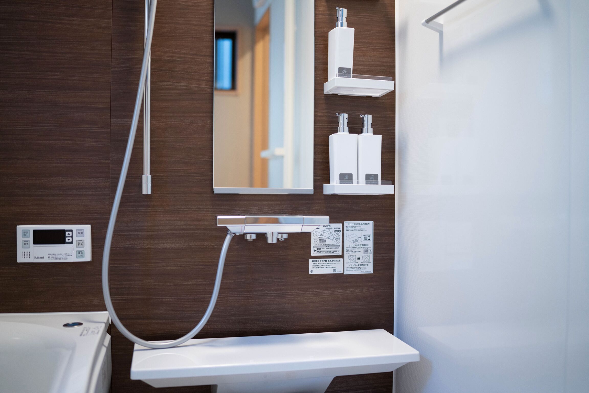 A bathroom with a wooden panel wall, a white sink, a mirror, and a shower control panel.