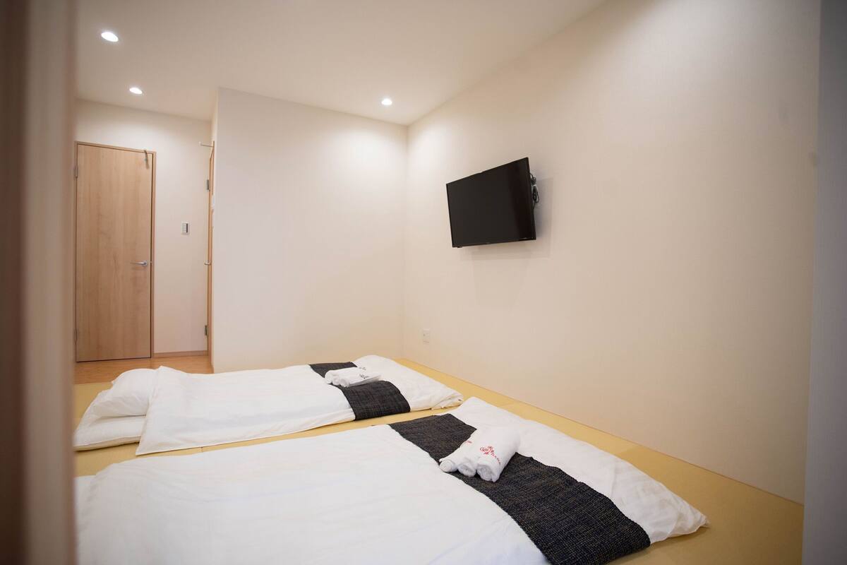A hotel room with two beds, a flat-screen TV mounted on the wall, and a wooden door.