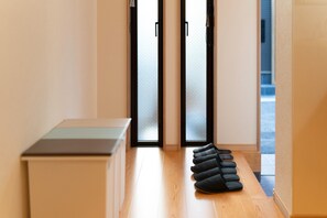 A hallway with a bench, a pair of sliding glass doors, and a row of black slippers on the floor. - HANASTAY MATSU (Osaka)