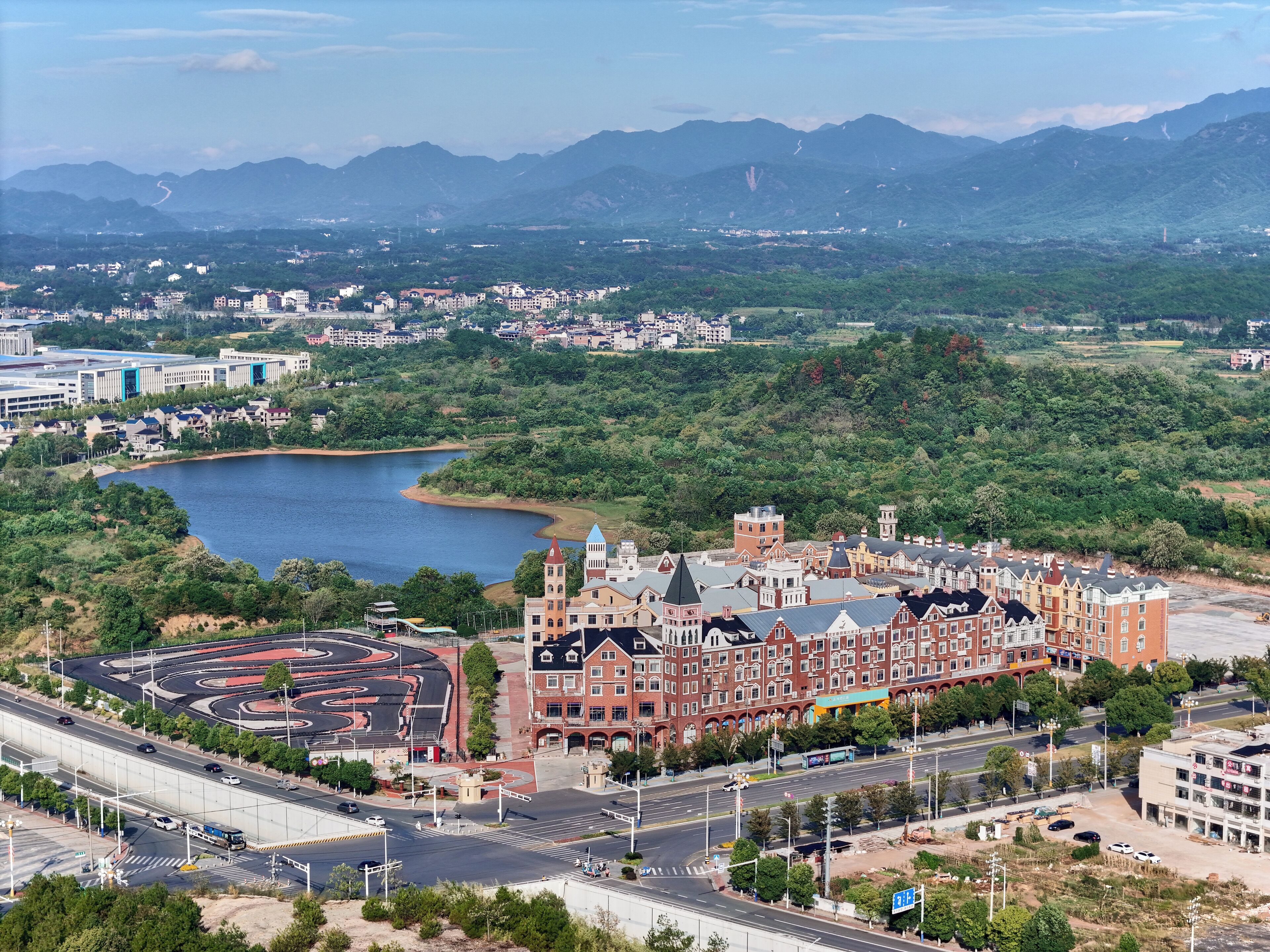 A large, historic building with a central tower, surrounded by a mix of modern and traditional architecture, set against a backdrop of mountains and a lake.