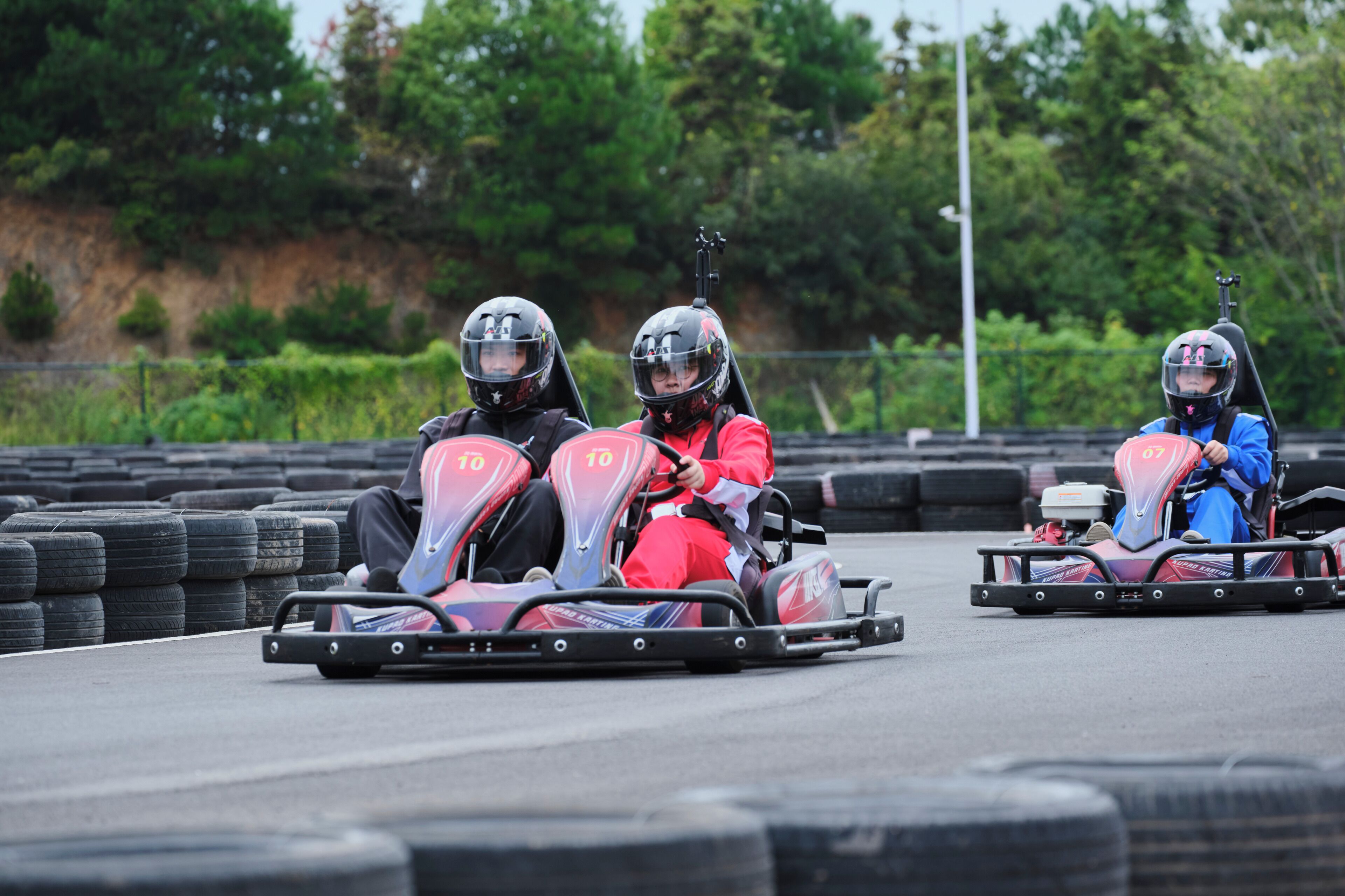 Tres karts de carreras en una pista, con neumáticos y una zona verde de fondo.