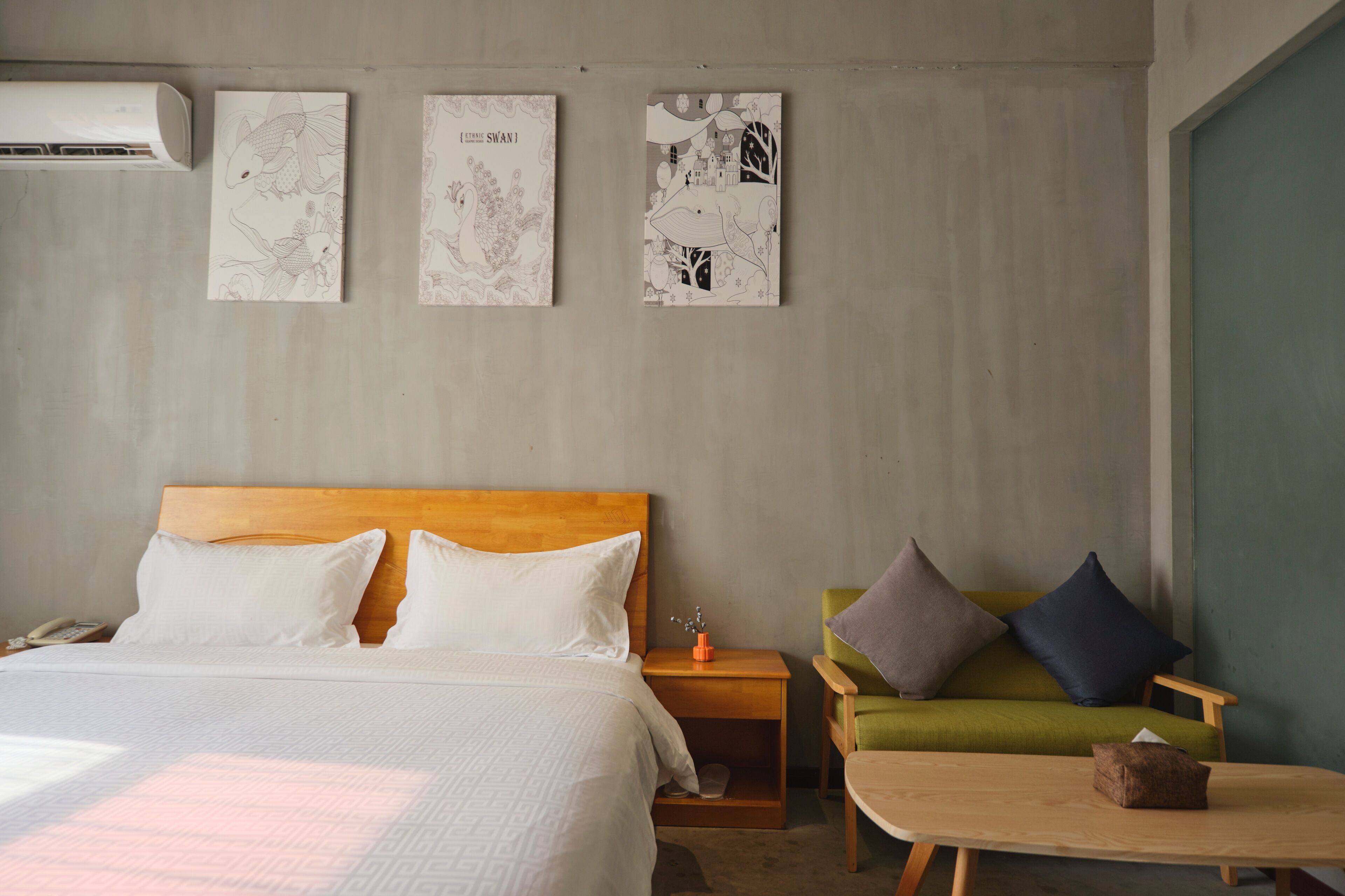 A hotel room with a wooden bed, a green sofa, a small table, and wall art.